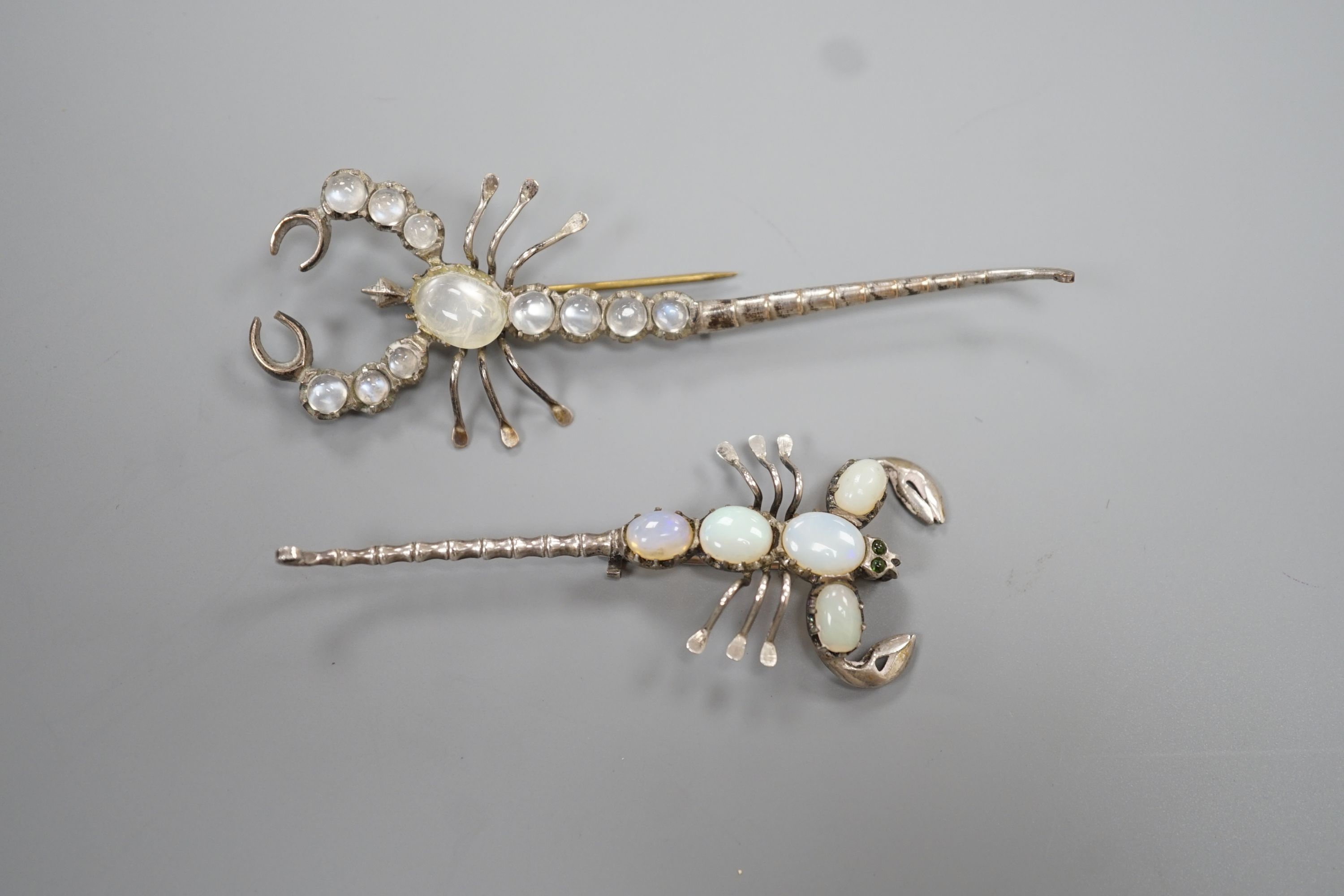 Two white metal scorpion brooches, one set with moonstones, the other with opals, largest 9cm.